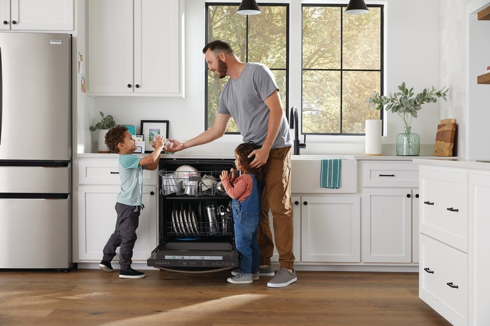 Father and kids standing in the kitchen in front of a full Dishwasher