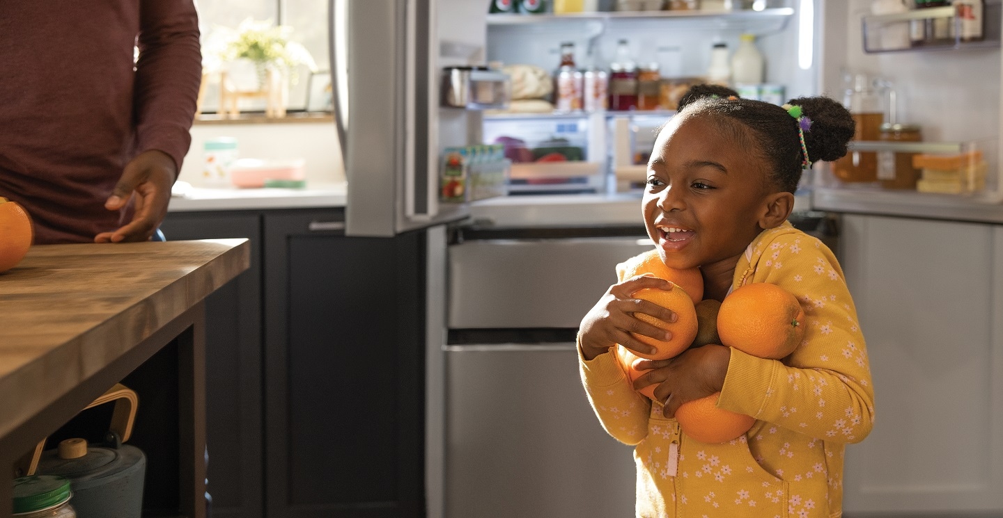 Girl in kitchen carrying oranges