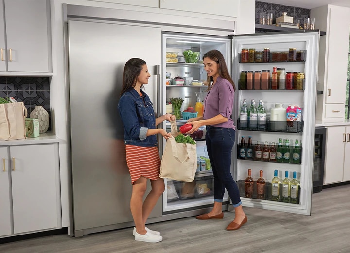 Two Women placing groceries into a full refrigerator